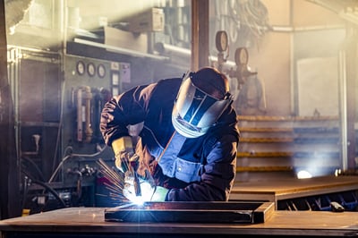 Soudeur avec un masque de protection et des vêtements de travail soude avec une machine à souder MIG-MAG.