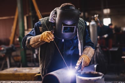 Soudeur à l'arc électrode enrobée et TIG en uniforme de protection et masque de soudure tuyau métallique sur la table industrielle.